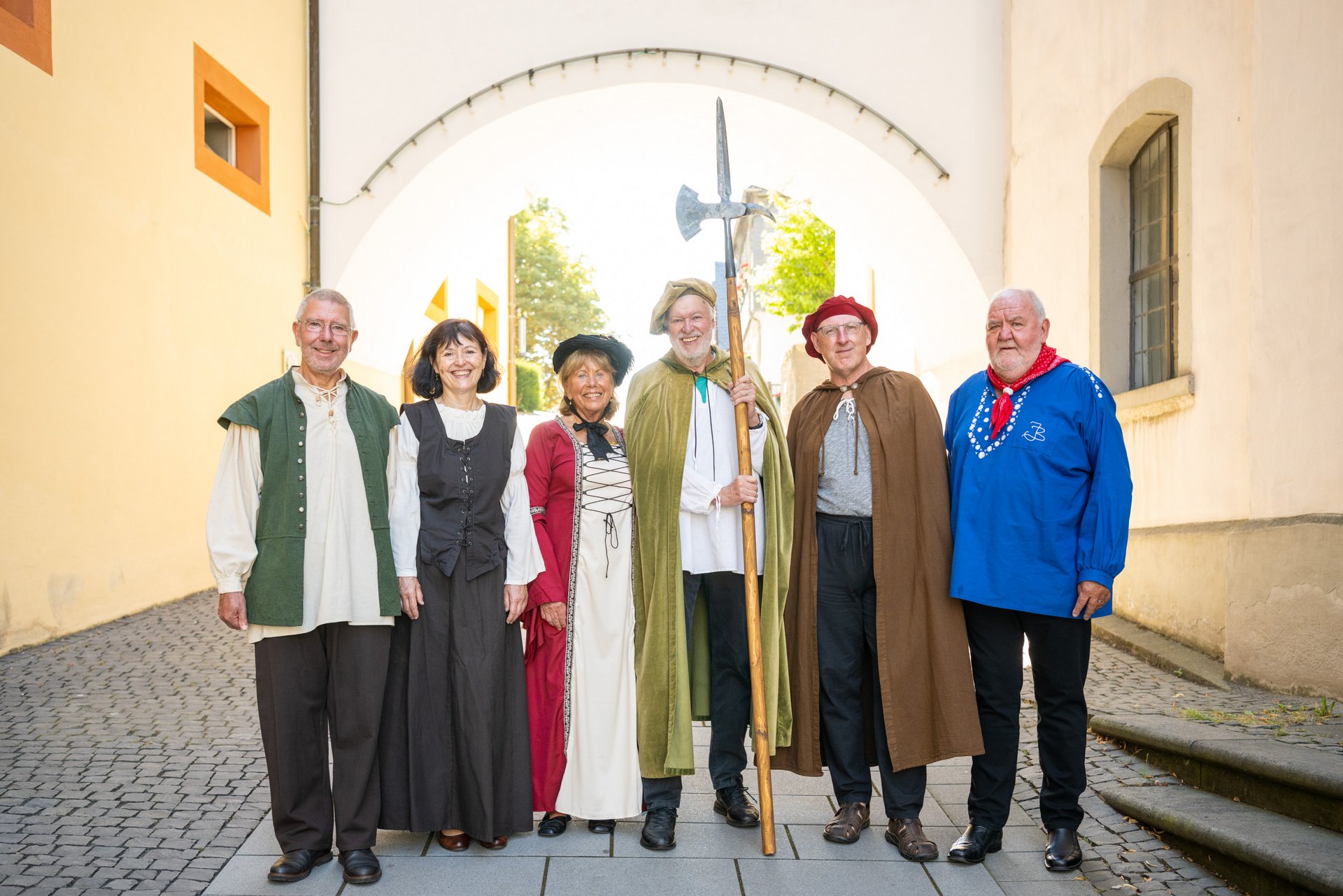 Sechs Stadtführer im historischen Gewand vor dem Torbogen zwischen Schloss und evangelischer Kirche