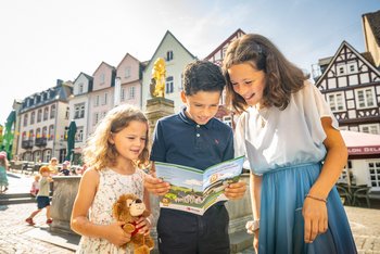 Drei Kinder lesen im Hachenburger Kinderstadtführer auf dem Alten Markt in Hachenburg