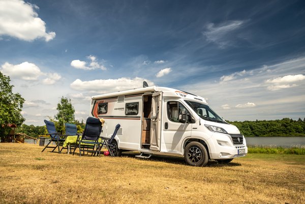 Camper mit Stühlen und Tisch davor im Hintergrund der Dreifelder Weiher