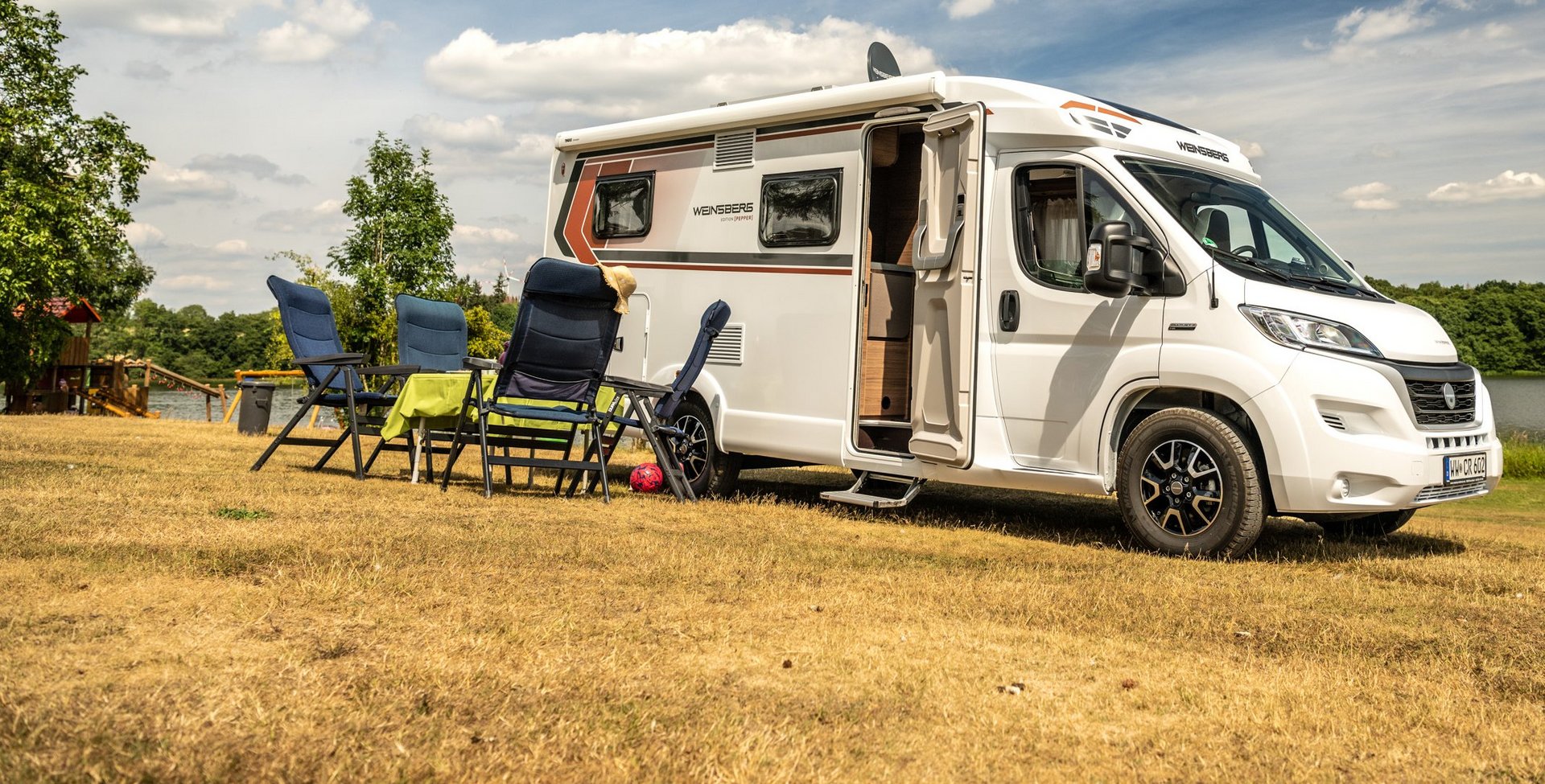 Camper mit Stühlen und Tisch davor im Hintergrund der Dreifelder Weiher