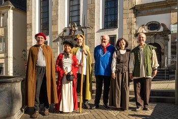 Sechs Stadtführer in historischen Gewändern vor katholischen Kirche am Löwenbrunnen