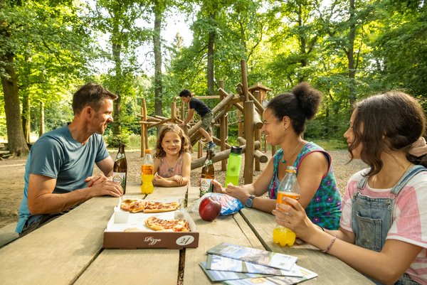 Familie macht Pause auf dem Waldspielplatz und isst Pizza