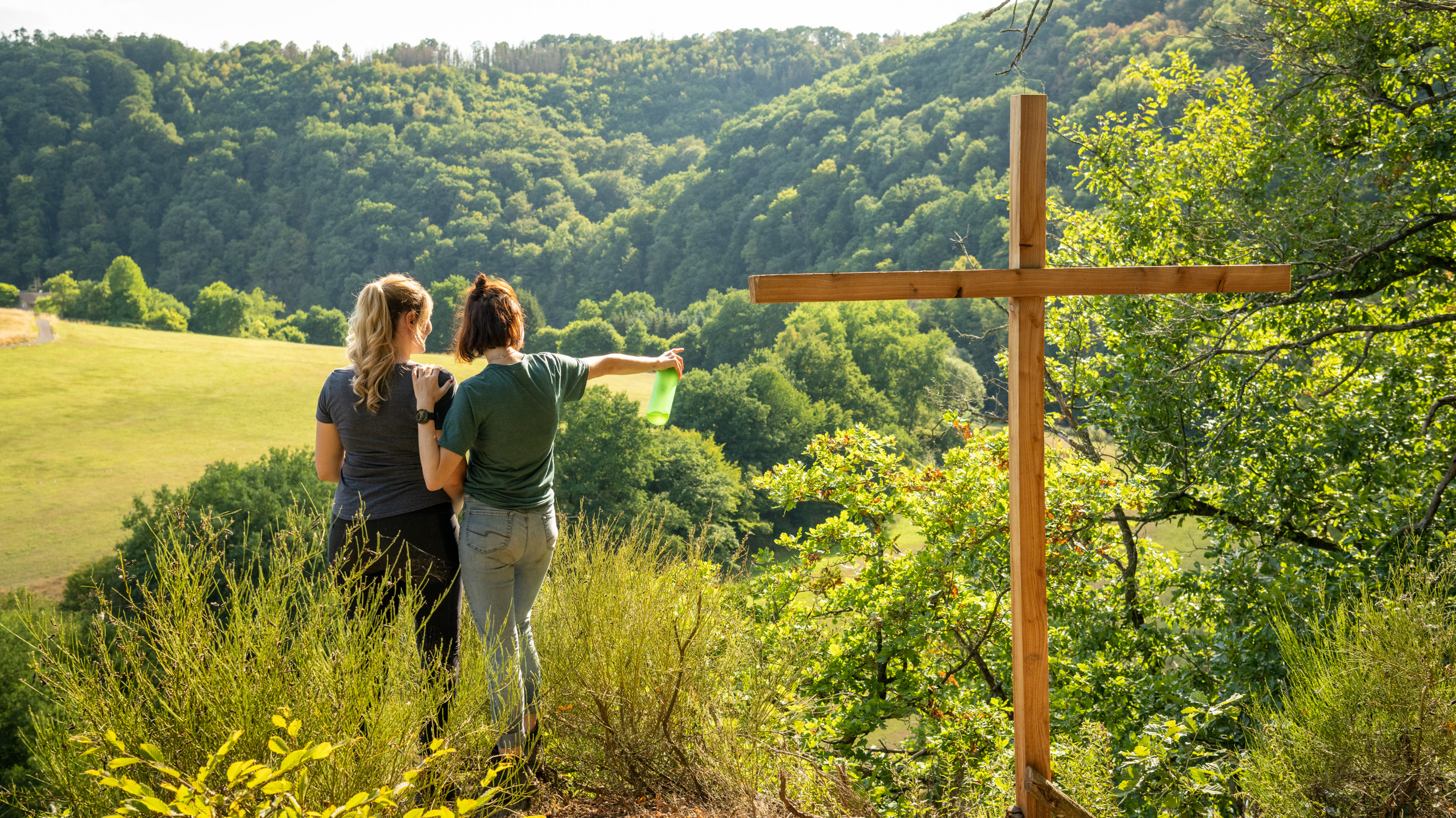 Wanderinnen stehen neben dem Kreuz am Weltendepfad und schauen in die bewaldete Ferne