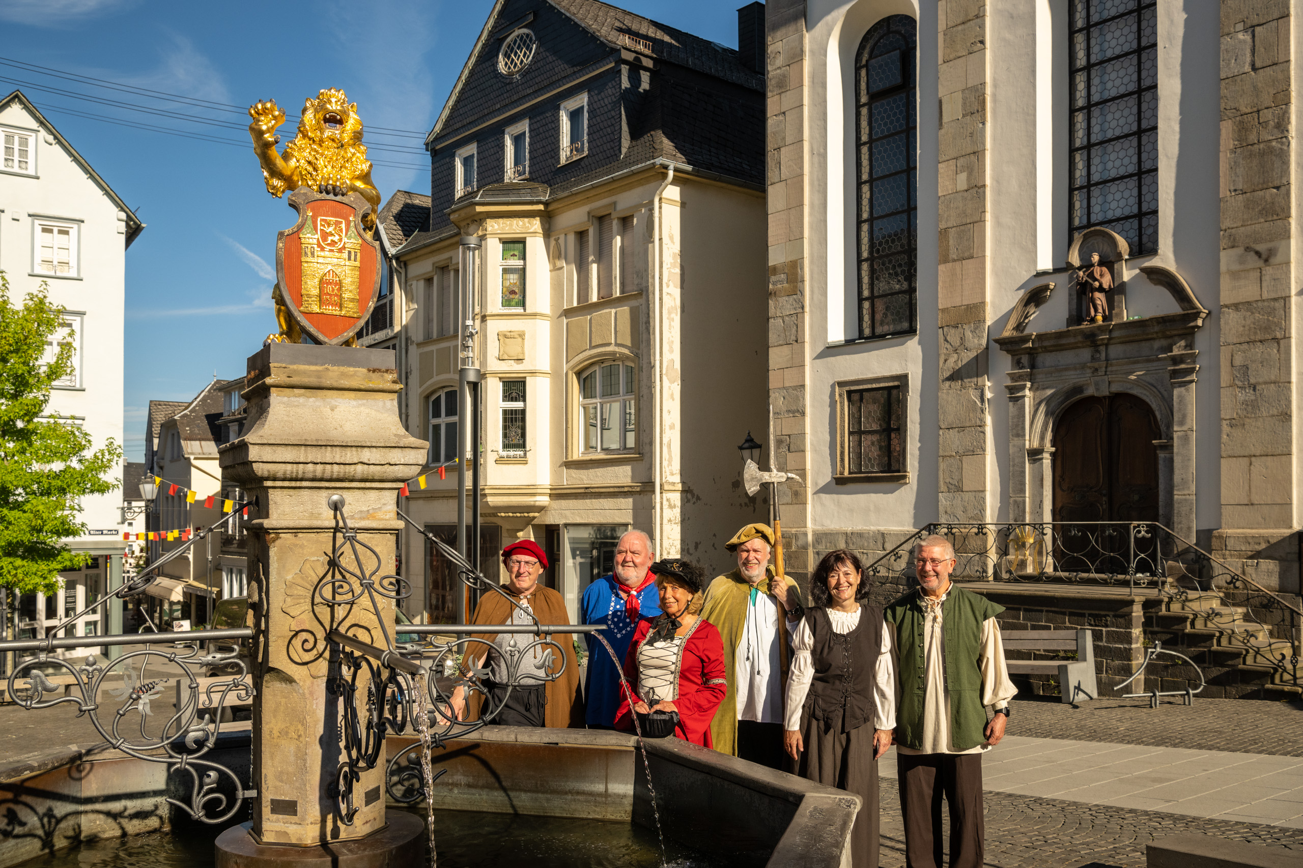 Fünf Stadtführer in mittelalterlichen Kostümen und Kirmeskittel stehen am Löwenbrunnen auf dem der goldene Löwe thront