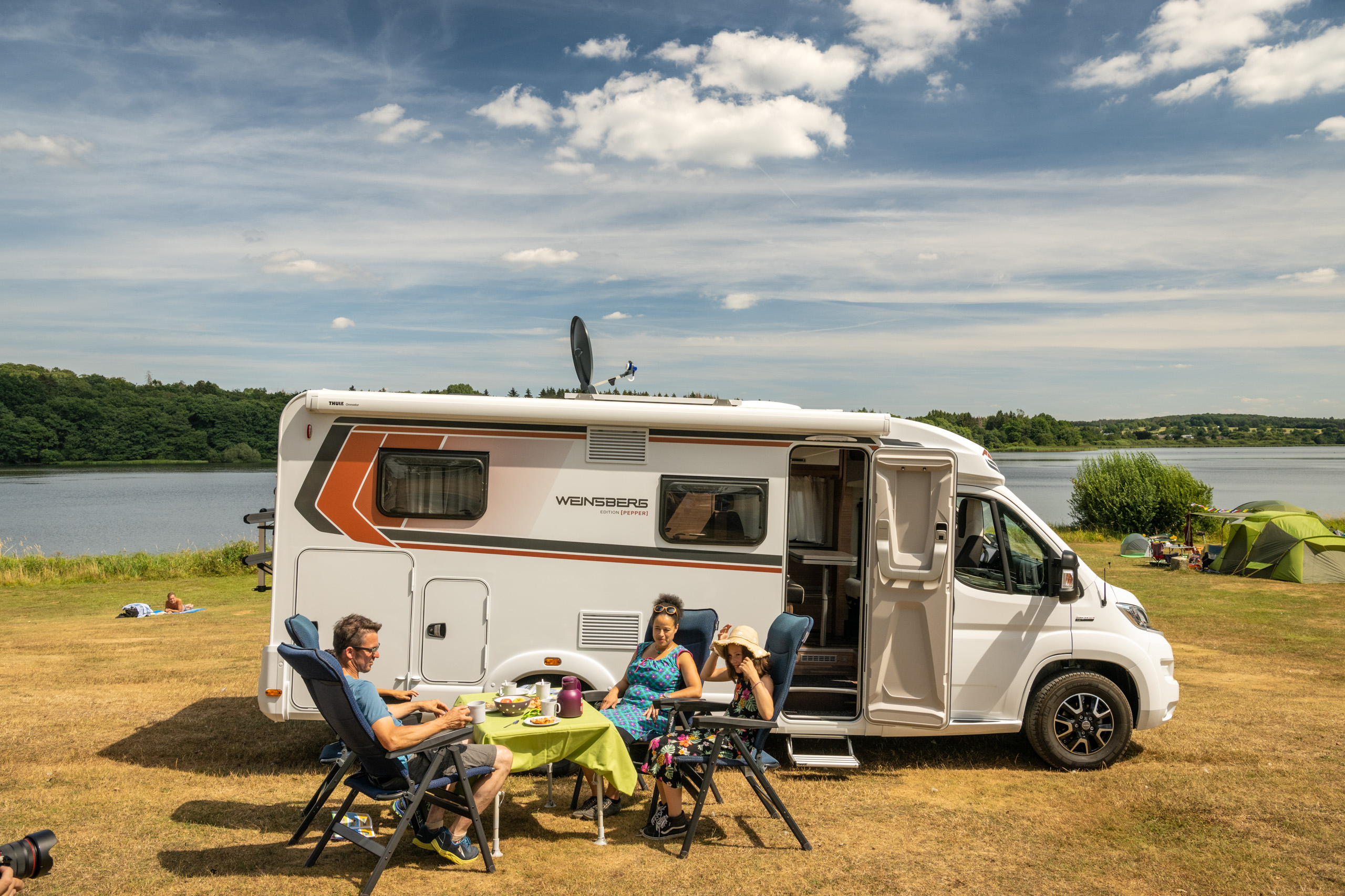 Familie sitzt vor ihrem Camper in der Sonne am Dreifelder Weiher